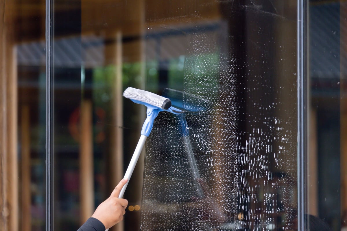 A person cleaning a window with a squeegee, removing streaks from the glass